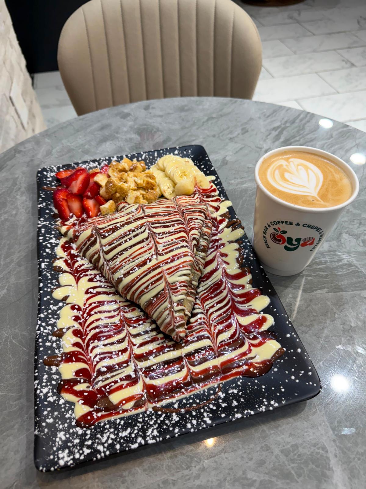 OYA crepe with strawberries and banana beside a latte in an OYA cup